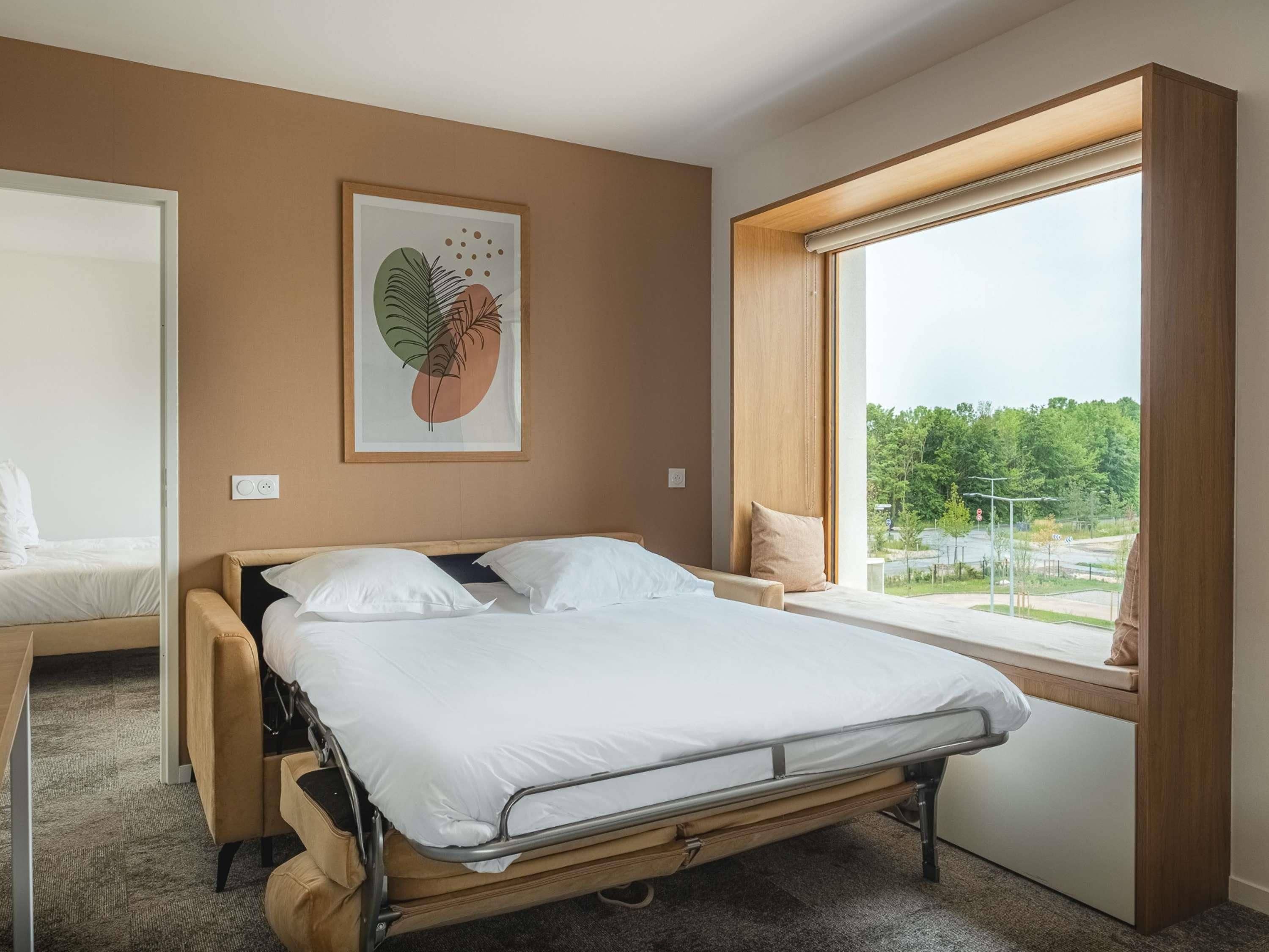 Une chambre d’hôtel avec un lit, une fenêtre donnant sur un beau paysage et une œuvre d’art accrochée au mur.