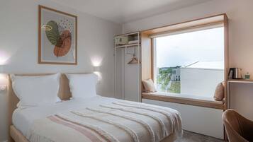 A bedroom with a bed, a window with a view, a wall-mounted shelf, and a framed picture.