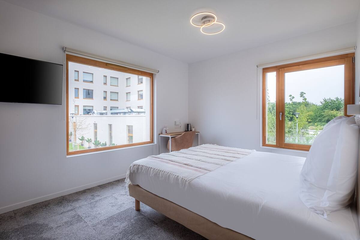 Ein Schlafzimmer mit einem Bett, einem Schreibtisch und zwei Fenstern.