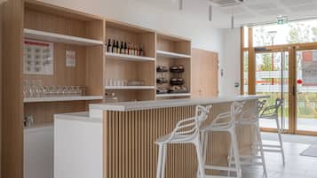 Een moderne bar met houten planken, glazen en flessen. Drie witte barkrukken en een bar staan er.