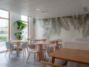 A modern cafe interior with round tables, chairs, and a large plant. - ibis Styles Amiens Sud (Amiens)