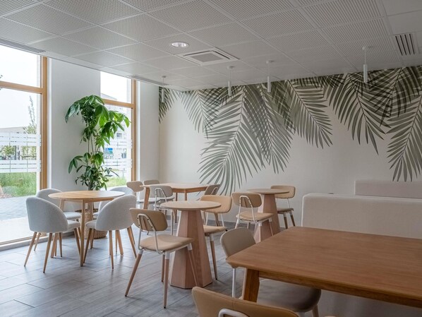 A modern cafe interior with round tables, chairs, and a large plant.