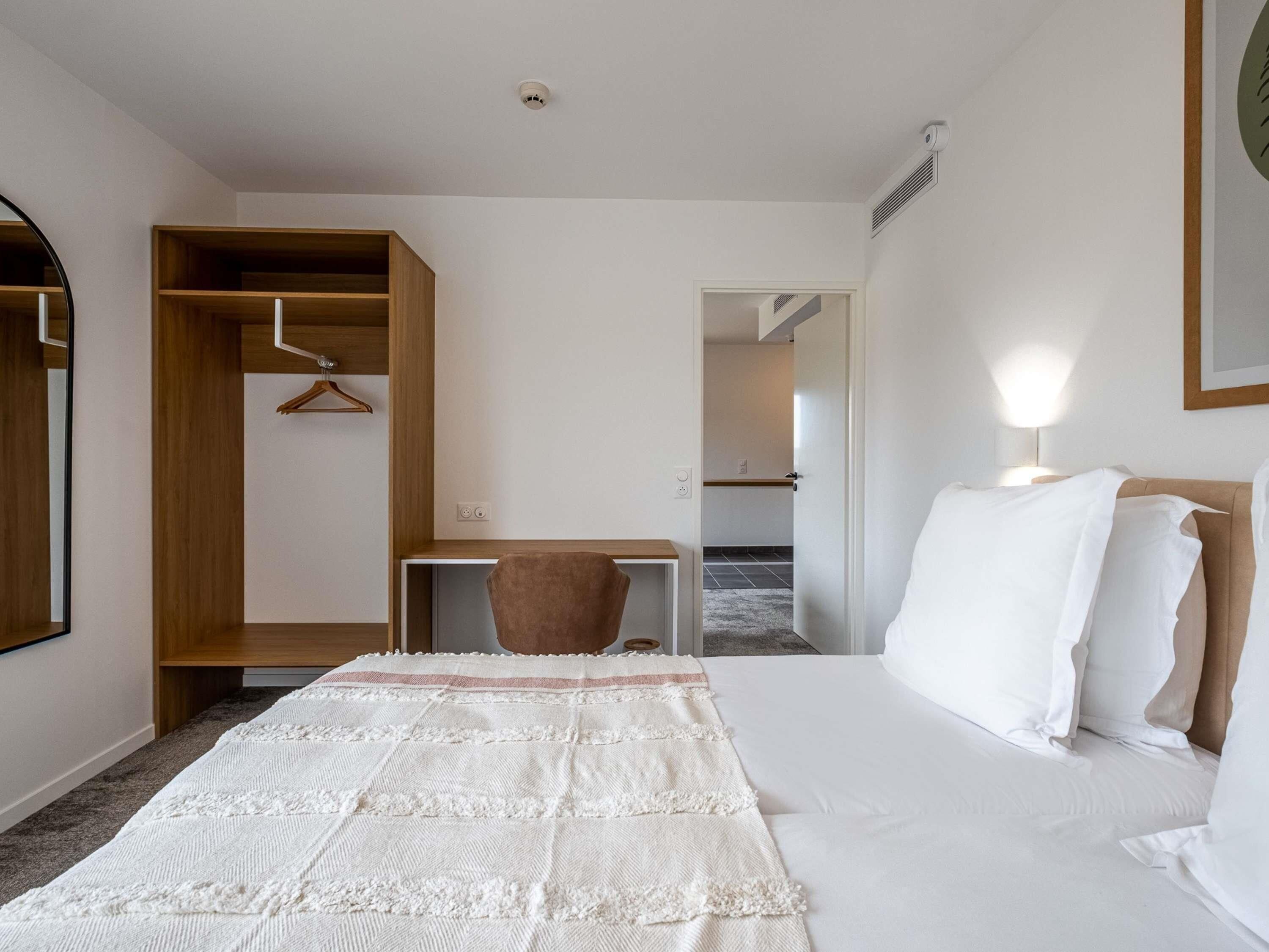 Ein Hotelzimmer mit einem Bett, einem Schreibtisch, einem Stuhl, einem Kleiderschrank und einem Spiegel.