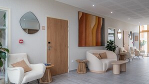 A modern hotel lobby with a large sofa, armchairs, a coffee table, and a wooden door. - ibis Styles Amiens Sud (Amiens)
