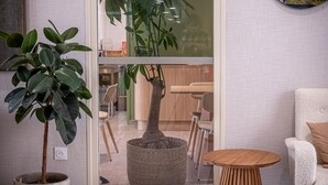 A modern living room with a large potted plant, a round wooden table, and a white armchair. - ibis Styles Amiens Sud (Amiens)