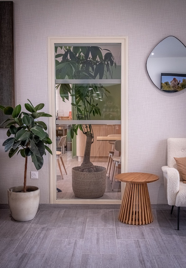 A modern living room with a large potted plant, a round wooden table, and a white armchair. - ibis Styles Amiens Sud (Amiens)