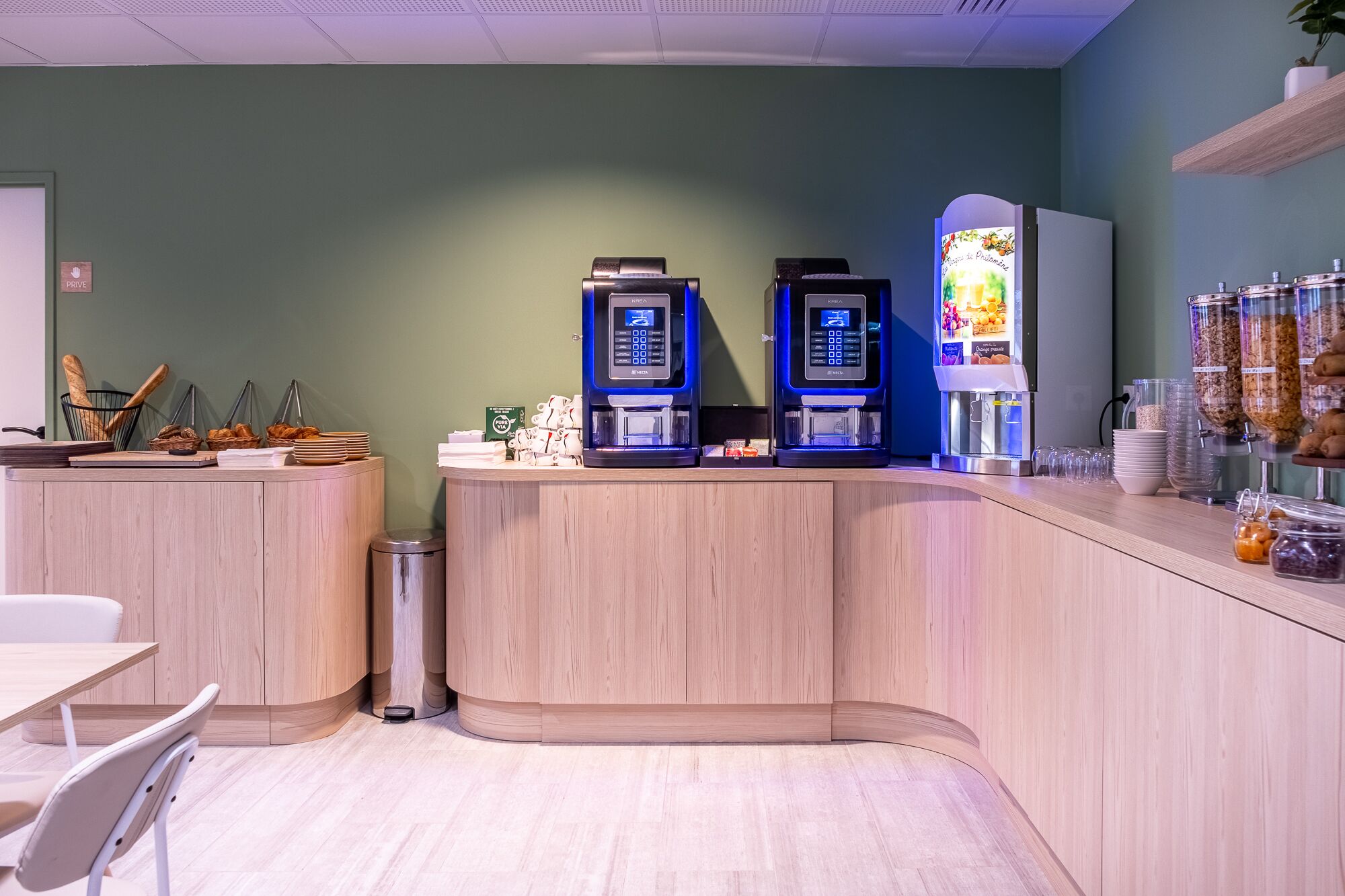 A cafe area with two espresso machines, a trash bin, and a counter with food items.