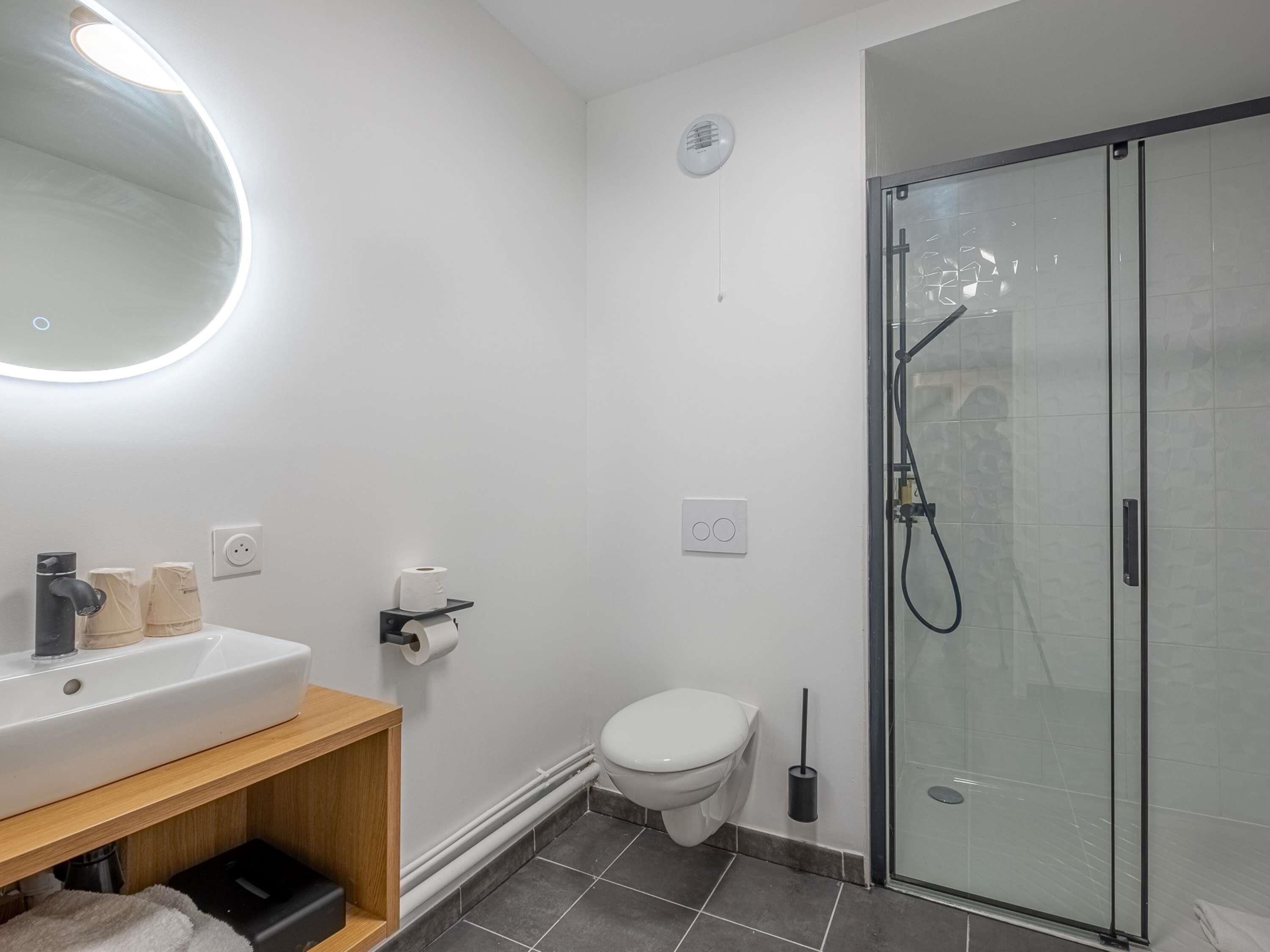 A modern bathroom with a white sink, toilet, and glass shower enclosure.