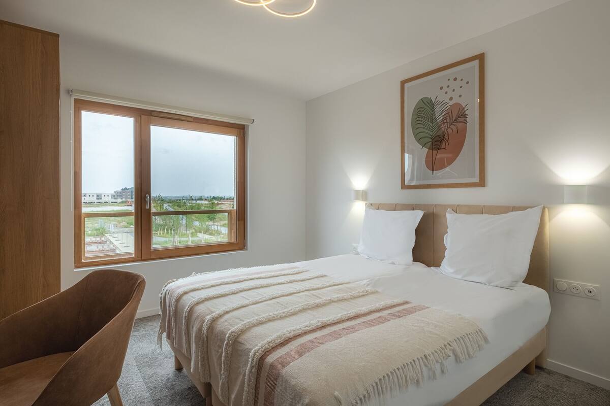 Ein Schlafzimmer mit einem großen Bett, einem Fenster mit Ausblick, einem Sessel und einer Wandleuchte.