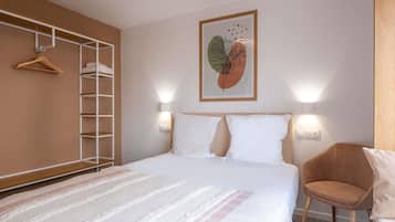 Una habitación de hotel con cama, armario, silla y lámpara fijada a la pared.