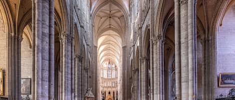 Interior de una catedral con altos techos abovedados, grandes columnas de piedra y filas de bancos de madera.