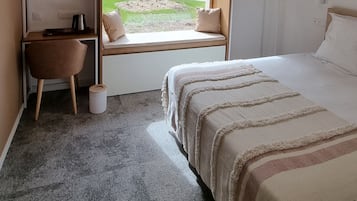 Una habitación de hotel con cama, escritorio, silla, ventana con vistas al exterior y lámpara en el techo.