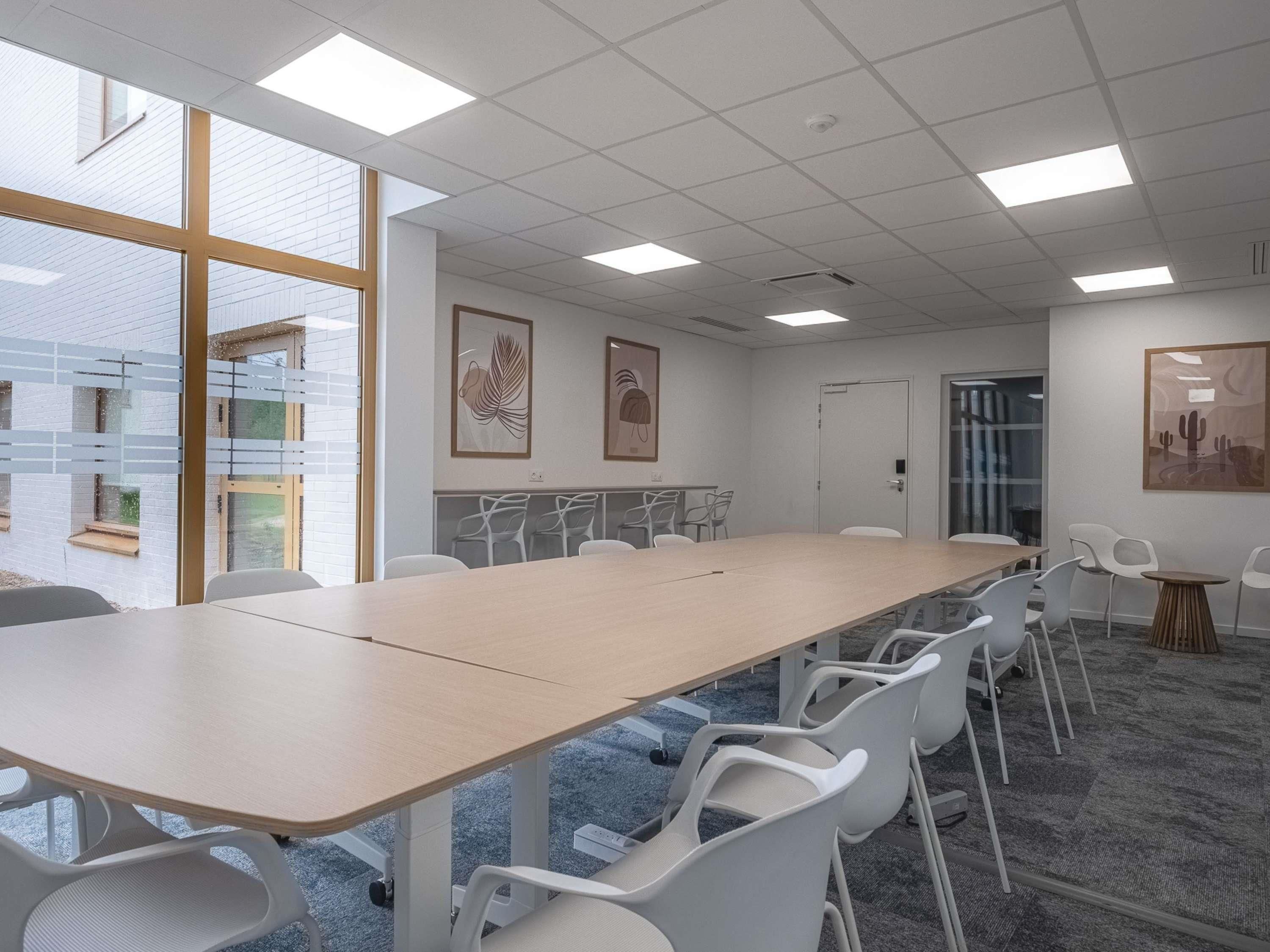 A conference room with a long table, white chairs, and artwork on the walls.