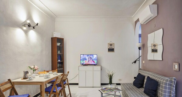 Un espacio habitable compacto con comedor, un sofá, un televisor y una mesita con revistas.
