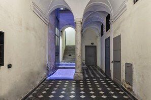 Un pasillo con piso a cuadros, paredes blancas y una escalera que lleva a un nivel superior.