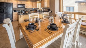 A modern kitchen with wooden cabinets, a central island, and a dining area with a wooden table set for four.
