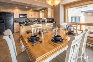 Una cocina moderna con armarios de madera, una isla central y un comedor con una mesa de madera dispuesta para cuatro personas.