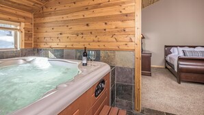 A wooden cabin interior with a hot tub, a bed, and a stone-tiled shower area.