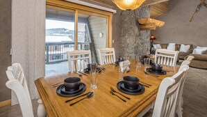 A dining area with a wooden table set for four, white chairs, and a view of a snowy landscape through large windows.