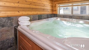 A wooden cabin interior with a hot tub, stone tiles, and a window with a view.