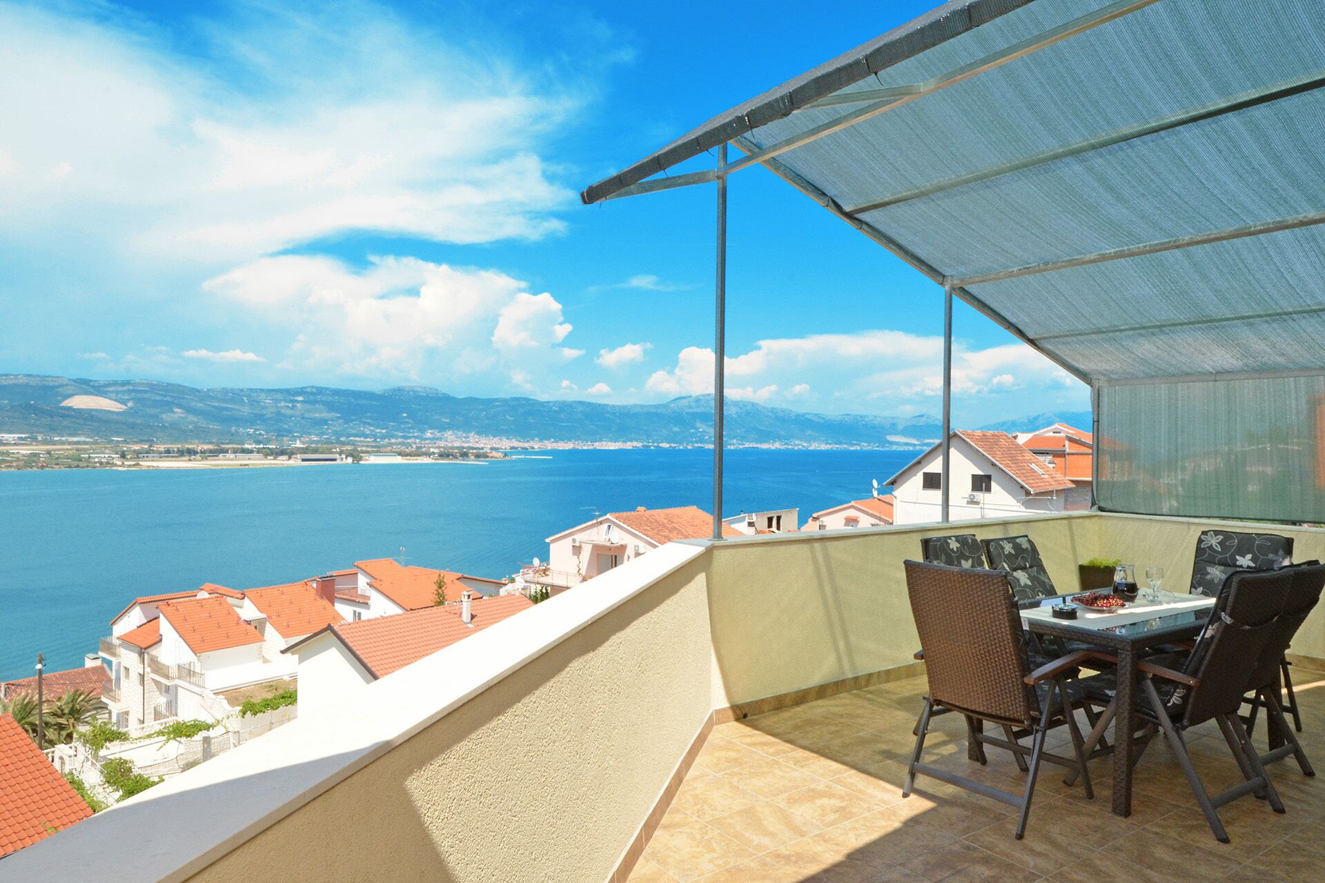 Un balcon avec une table et des chaises, offrant une vue sur la côte, avec des bâtiments et une étendue d’eau.
