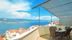 Ein Balkon mit Tisch und Stühlen, der Blick auf die Küste mit Gebäuden und einem Gewässer bietet.