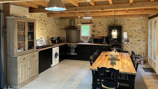 A rustic kitchen with wooden beams, a wooden dining table, and a washing machine. - Stone country house with swimming pool (Villefranche-du-Périgord)
