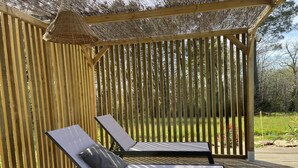 A wooden deck with two lounge chairs and a pergola with a woven roof. - Stone country house with swimming pool (Villefranche-du-Périgord)