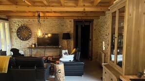 A cozy living room with a stone wall, wooden ceiling, a black sofa, a wooden cabinet, and a fireplace. - Stone country house with swimming pool (Villefranche-du-Périgord)