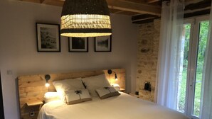 A bedroom with a wooden headboard, a large bed with white bedding, a hanging lamp, and a stone wall. - Stone country house with swimming pool (Villefranche-du-Périgord)