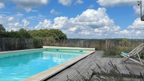A swimming pool with a wooden deck and a view of a forested area in the background. - Stone country house with swimming pool (Villefranche-du-Périgord)