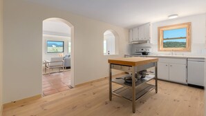 Une cuisine moderne avec des meubles blancs, une table en bois et une vue sur un paysage verdoyant par la fenêtre.