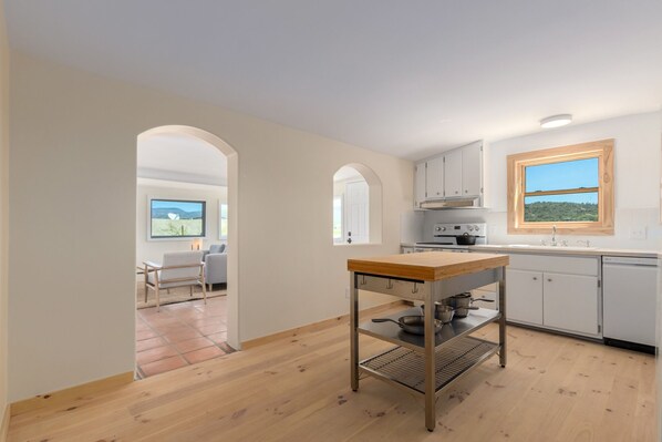 A modern kitchen with white cabinets, a wooden table, and a view of a green landscape through a window. - Private,romantic and charming mid-century cottage with panoramic views (Cave Creek)