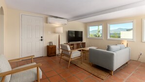 Un salon comprenant un téléviseur, un canapé et des fauteuils, une porte et une fenêtre donnant sur les montagnes.