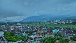 A densely populated urban area with buildings and green fields under a cloudy sky. - Shivoham Yoga Retreat - Spacious and Fully Equipped Apartment in Tranquil Area (Rishikesh)