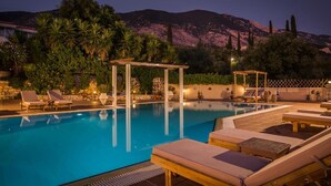 A swimming pool with lounge chairs and a pergola, surrounded by greenery and mountains in the background.
