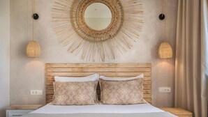 A bedroom with a wooden headboard, two patterned pillows, a round mirror, and two wall-mounted lamps.