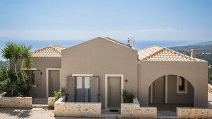 A modern villa with a flat roof, stone walls, and a view of the sea.