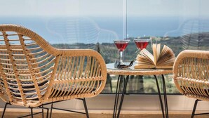 A wicker chair and table set on a balcony with a view of the ocean.