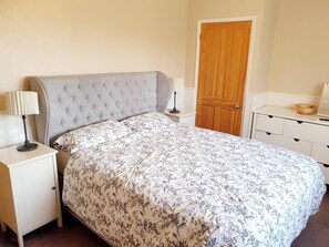 A bedroom with a tufted headboard, floral bedspread, bedside tables with lamps, a wooden door, and a white dresser. - Spacious 3bed Property With Parking Large Garden (South Ockendon)