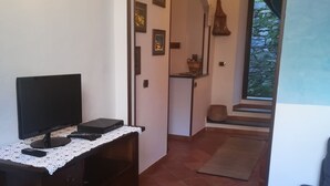 Een kamer met een donker houten bureau, een flatscreen-tv en een wit tafellaken. Er ligt een betegelde vloer en is een deur naar een balkon met uitzicht op een stenen muur.