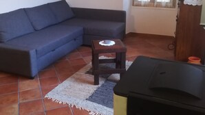 Een woonkamer met een blauwe bank, een klein houten tafeltje en een betegelde vloer.