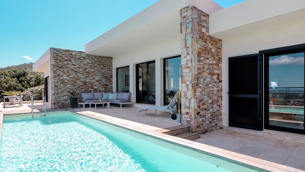 A modern outdoor pool area with a stone wall, lounge chairs, and a clear view of the sea. - Villa with pool, sea view (Borgo)