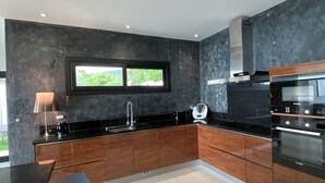 A modern kitchen with dark cabinetry, a black countertop, and stainless steel appliances. - Villa with pool, sea view (Borgo)