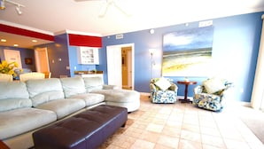 A living room with a sectional sofa, two patterned armchairs, a dark leather ottoman, and a large painting on the wall. - Ocean's Edge 403-Oceanfront 9th St, Free WiFi, Elev, W/D, AC (Ocean City)