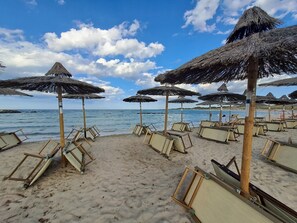 Een strand met rieten parasols en ligbedden.