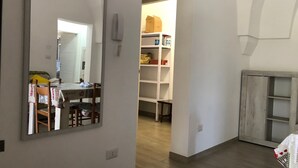 Une pièce avec un plancher en bois, un mur blanc, un miroir, une petite table avec une chaise et un meuble en bois.