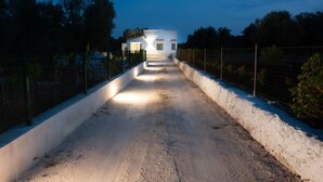 Un chemin mène à un bâtiment blanc doté d’un toit en pente, entouré d’une clôture et d’arbres.