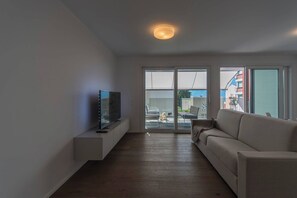 Un salon moderne avec un téléviseur à écran plat posé sur une étagère intégrée, un canapé et une porte-fenêtre coulissante donnant sur un espace extérieur.