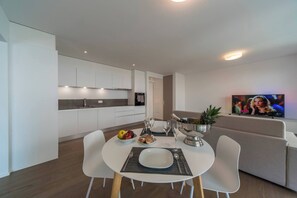A modern kitchen with white cabinets, a dining table with chairs, a TV on the wall, and a sofa in the living area. - Vacation Rental City 10 in Massagno (Massagno)
